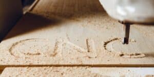 Close-up of a CNC (Computer Numerical Control) machine carving the letters ‘CNC’ into a wooden surface, highlighting precision woodworking technology.