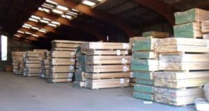 Stacks of European Oak timber planks neatly organized in a warehouse with natural light filtering through roof vents.
