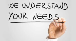 Hand holding a marker writing ‘WE UNDERSTAND YOUR NEEDS’ on a clear surface with a white background, emphasizing customer service and business commitment.