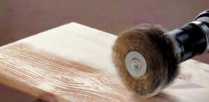 Electric orbital sander smoothing a wooden plank, creating sawdust, in a woodworking project.