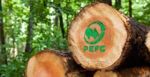 A stack of cut logs in a forest, with the PEFC logo and acronym marked in green on the end of one log.