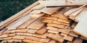 A stack of wooden planks of various sizes and thicknesses piled on top of each other, placed outdoors on a grassy area.