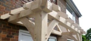 Close-up view of a wooden canopy structure attached to a brick house, showing detailed joinery and craftsmanship
