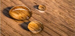 Three water droplets on a wooden surface, each reflecting the wood grain pattern.